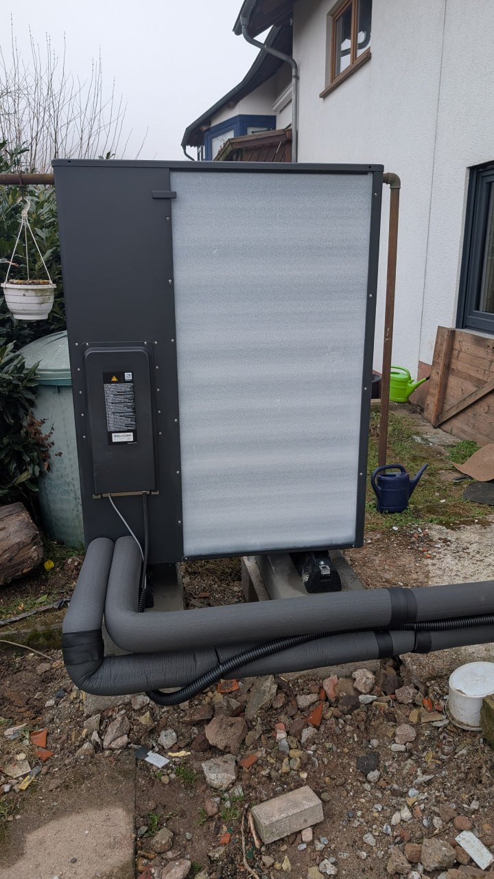 Heat pump unit installed outside a German home with insulated pipes